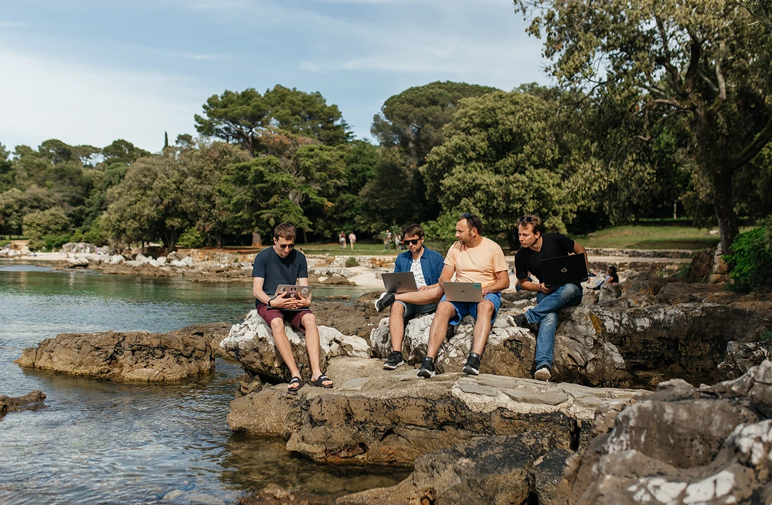 Four Go Wombat team members working on laptops on the rocks by the sea